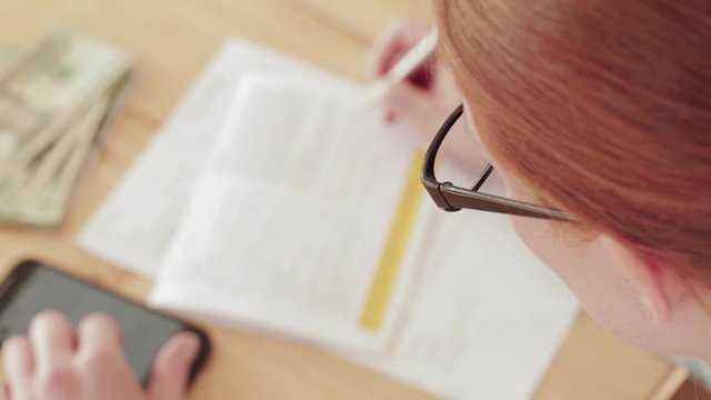 A young woman fills out a paper form at home. Top view with shallow DOF, static footage.