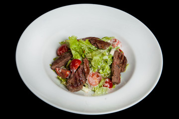 Veal salad, salad with large slices of veal and fresh vegetables on a plate on a black background
