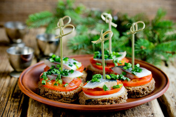 Canapes with rye bread, salted herring fillet, mustard, onion, tomato and skewers on plate