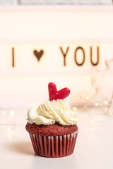 I love you written on a decorative lamp next to red cupcakes, red velvet with mascarpone cream. Valentine's day concept