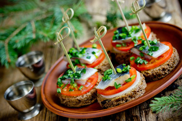 Canapes with rye bread, salted herring fillet, mustard, onion, tomato and skewers on plate