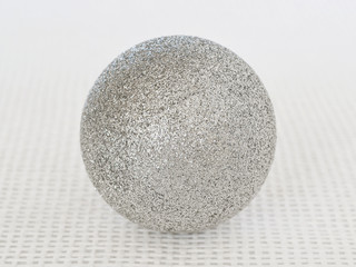 One shiny silver christmas ball with sparkles on a white textural background close up