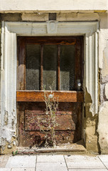 Tür von verlassenem, baufälligem Haus und vor der Tür wächst Unkraut