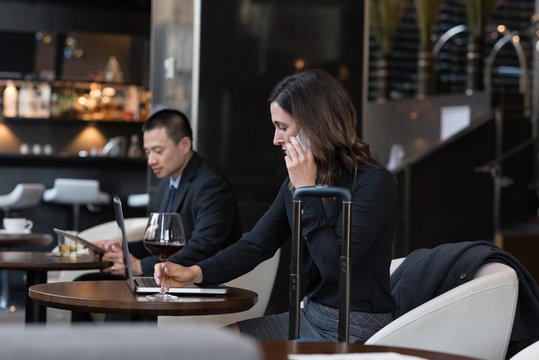 Businesswoman having red wine while talking on mobile phone