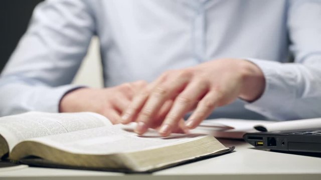 A young Christian female student reads the Bible, takes notes and writes on a laptop. Dolly move shot with follow focus.