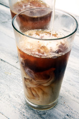 Ice coffee on a rustic table with cream being poured into it showing the texture and refreshing look of the drink