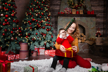 Obraz na płótnie Canvas Young mother female woman playing with son child kid in red sweater at home near decorated Christmas tree and fireplace during winter holidays. Merry Christmas and Happy New Year concept,