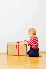 Cute baby opening a big box Christmas present. No retouch, closeup, studio lighting.
