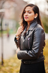 Close up portrait of pretty indian girl in black saree dress and leather jacket posed outdoor at...