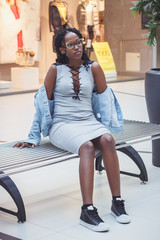 Young dark-skinned woman dressed in casual clothes on the bench in the mall