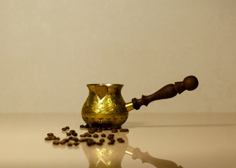 Cezve on a glass surface with coffee beans and reflection. Bronze item