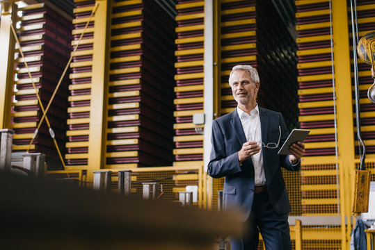 Successful entrepreneur standing in his company, using digital tablet