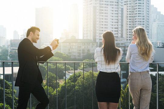Businessman taking picture of his female colleagues on city rooftop