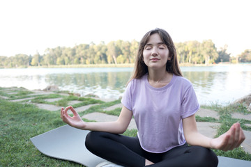 Fototapeta na wymiar Young beautiful woman doing yoga exercises in park on the bank river.