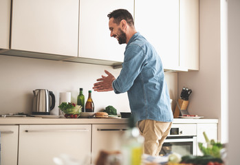 Side view portrait of handsome gentleman in denim shirt feeling happy while cooking at home