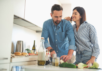 My hero. Waist up portrait of charming woman standing close to bearded man and looking at him with smile. Gentleman chopping onion in kitchen