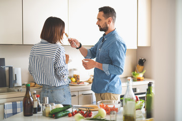 Wonderful aroma. Portrait of charming lady checking scent of red wine while standing with bearded gentleman in kitchen