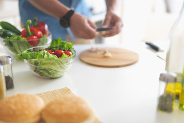 Healthy food. Close up of bowls with tomatoes, lettuce, cucumber and red bell pepper on kitchen table. Male hands with knife on blurred background