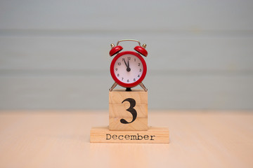 December 3rd set on wooden calendar and red alarm clock with blue background.