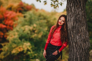 Beautiful girl in red leather jacket in autumn forest.