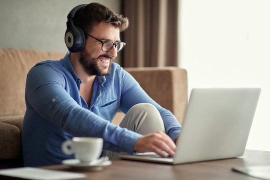 Smiling man with headphones using laptop in his home.