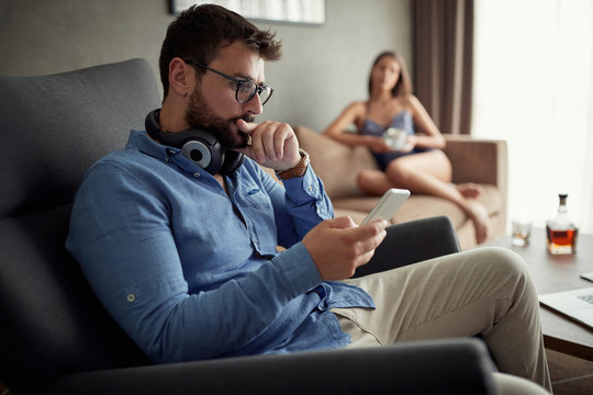 man using a phone and typing message while sitting on sofa at home.