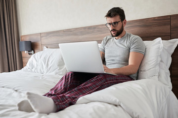 Man working in bed on laptop early in the morning.