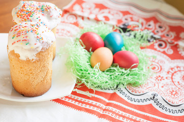 Beautifully decorated cupcakes in a plate. Easter cakes on a plate and the bright colored Easter eggs. Painted chicken eggs are in artificial decorative straw. Festive symbol on the table.