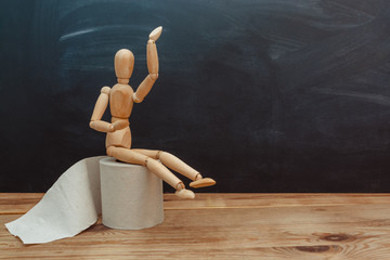 Wooden figure sit on a roll of toilet paper. Concept of the problem with digestion.