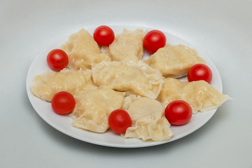 Dumplings and tomatoes on a white round plate.
