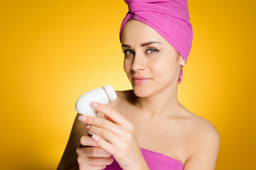 attractive young girl with a pink towel on her head holds an electric brush for deep cleansing of the skin on her face