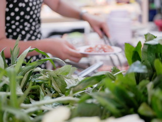 Selective focus of vegetables with woman hands picking pork in the background at a buffet hotpot restaurant