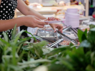 Obraz na płótnie Canvas Woman's hands taking pork from tray at a buffet hotpot ( Moo Joom ) restaurant with a defocus vegetables in the foreground