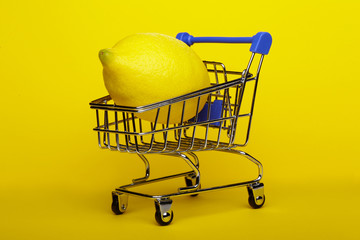 Lemon in shopping cart, shopping trolley on yellow background