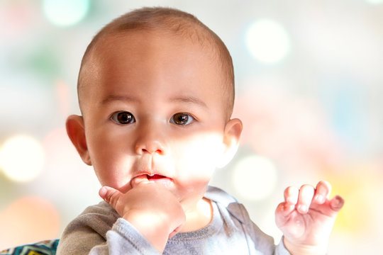 Cute baby boy with his finger in his mouth looking at the camera with shallow depth of field