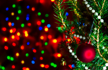 Fototapeta na wymiar Red Christmas ball on Christmas tree with blurred lights. Christmas ball and lights on dark blur background. Christmas card with blurred lights. Background with bokeh of Christmas lights. Copy space.