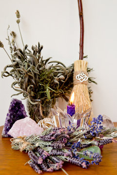 Purple beeswax candle, besom and dried herbs on altar with crystals