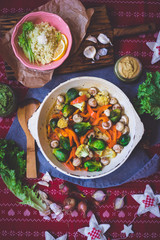 Baked roasted vegetables for Christmas lunch or dinner on red tablecloth. Vegan food with brussels sprouts, carrots, cauliflower, mushrooms. Social network trendy color style. Cast iron skillet pan