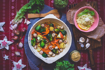 Baked roasted vegetables for Christmas lunch or dinner on red tablecloth. Vegan food with brussels sprouts, carrots, cauliflower, mushrooms. Social network trendy color style. Cast iron skillet pan