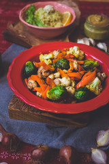 Baked roasted vegetables for Christmas lunch or dinner on red tablecloth. Vegan food with brussels sprouts, carrots, cauliflower, mushrooms. Social network trendy color style. In red bowl or plate