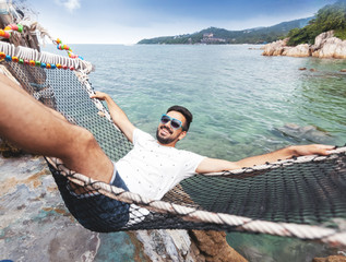 Attractive handsome young latin brunette man with a beard on a hammock on vacation against the...