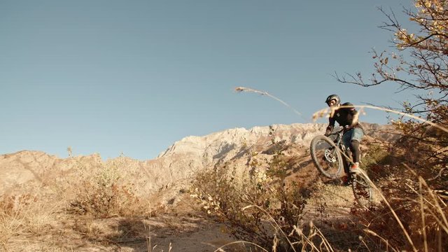 Mountain cycler riding up the path in mountains in sunset, following the trail or road, then doing cool jump - extreme, fitness,
