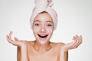 surprised happy girl with a towel on her head puts on the face nourishing cream