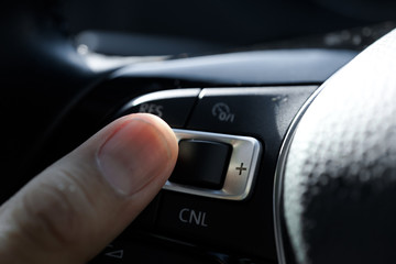 A man hand finger operating the Auto Cruise function in a modern car