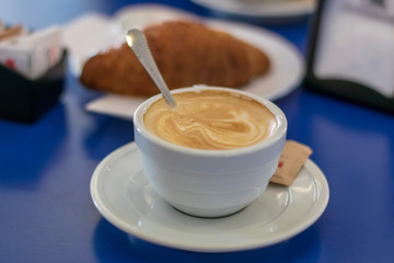 cup of coffee with cream and a croissant 