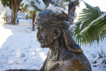 Fototapeta na wymiar Urban landscape with sculpture on the background of snow and palm trees.