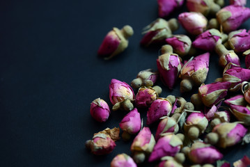 Dried rose buds scattered on a dark surface close up