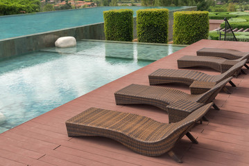 brown rattan sofa bed or bench, chair beside beautiful swimming pool, decorated with green bush of...