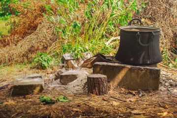 Fototapeta premium Old copper pot for cooking standing on concrete bricks on top of fireplace in the backyard