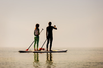 Silhouette of young happy couple doing paddle yoga